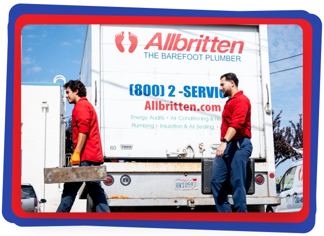 Two workers in red shirts carry toolboxes while walking past a white Allbritten plumbing service truck parked outside. The company logo and contact information are visible on the truck’s rear door.