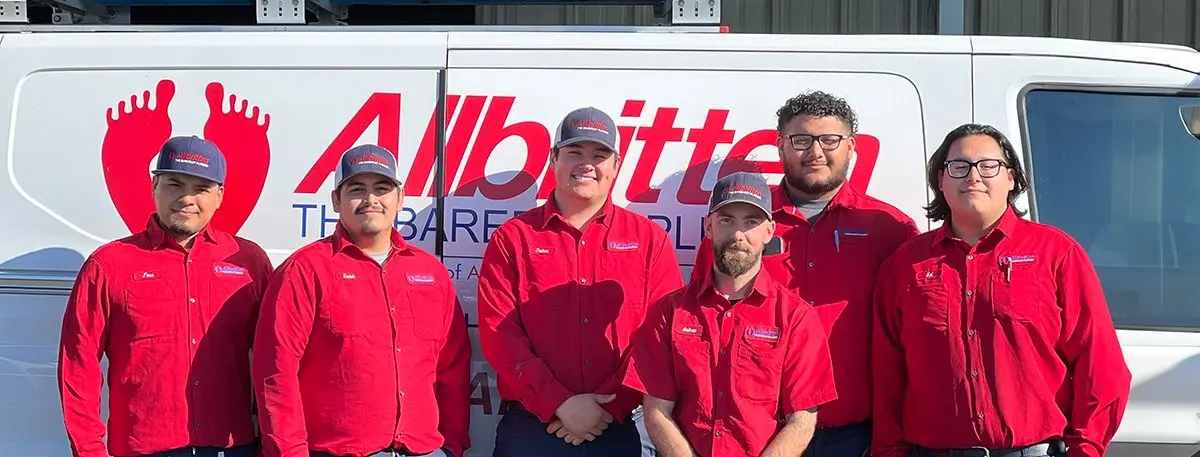 Five Allbritten employees in red work shirts and hats standing in front of a white company van.