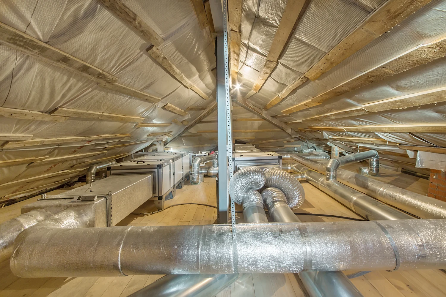 An attic with exposed wooden rafters, insulation, and complex ductwork for an HVAC system.