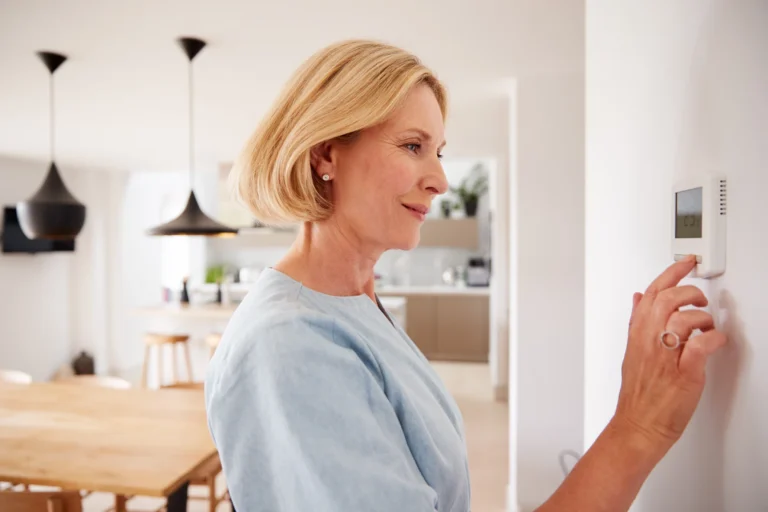 Woman adjusting a digital thermostat on a wall.