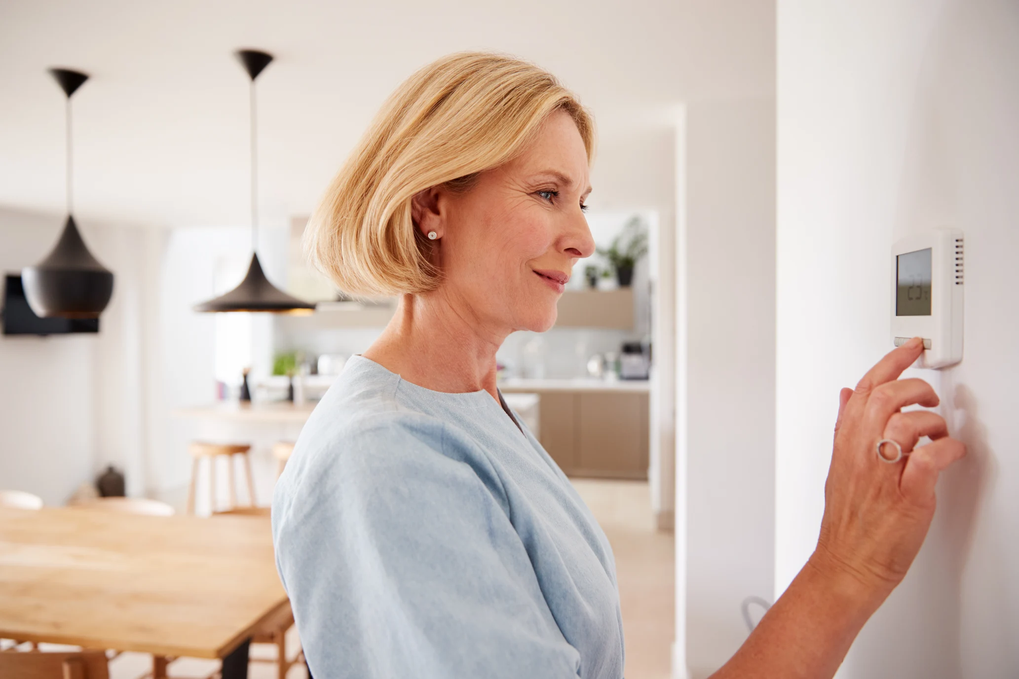 Woman adjusting a digital thermostat on a wall.